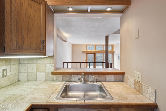 kitchen with a textured ceiling, brown cabinets, backsplash, and a sink