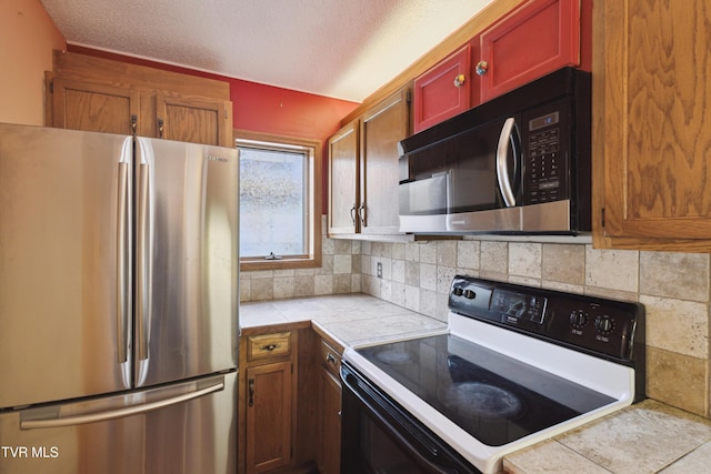 kitchen featuring decorative backsplash, electric range, freestanding refrigerator, and tile countertops