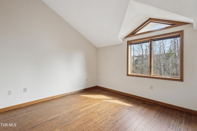 empty room featuring light wood-type flooring, visible vents, a textured ceiling, baseboards, and vaulted ceiling