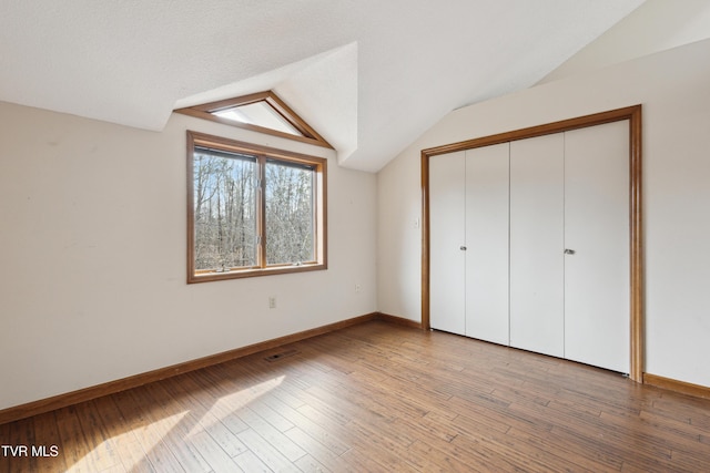 unfurnished bedroom with light wood-type flooring, baseboards, a closet, and vaulted ceiling