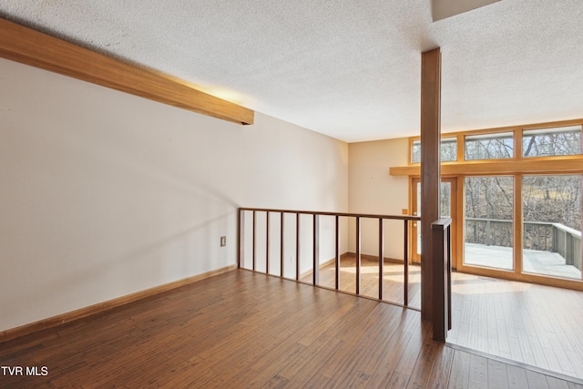 empty room featuring baseboards, wood-type flooring, and a textured ceiling