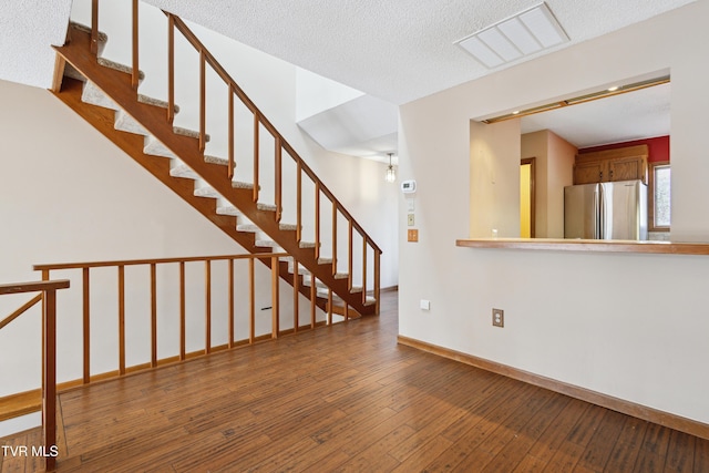 unfurnished living room with stairway, baseboards, visible vents, hardwood / wood-style flooring, and a textured ceiling