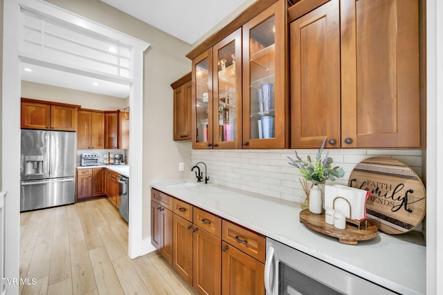 kitchen featuring brown cabinets, a sink, appliances with stainless steel finishes, light wood finished floors, and decorative backsplash