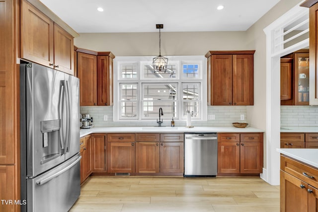 kitchen featuring light countertops, brown cabinets, appliances with stainless steel finishes, an inviting chandelier, and a sink