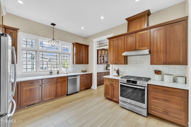 kitchen with light wood finished floors, under cabinet range hood, light countertops, appliances with stainless steel finishes, and a sink