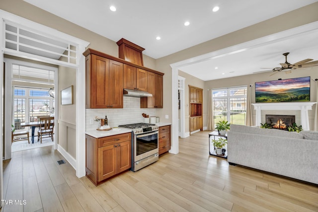 kitchen with light wood finished floors, open floor plan, under cabinet range hood, stainless steel gas range oven, and tasteful backsplash