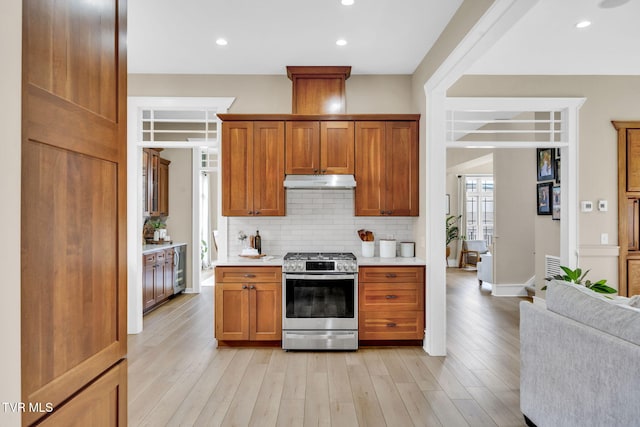 kitchen featuring backsplash, under cabinet range hood, light wood-type flooring, light countertops, and stainless steel gas stove