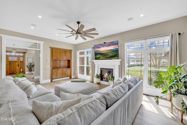 living area featuring light wood finished floors, a glass covered fireplace, recessed lighting, and ceiling fan