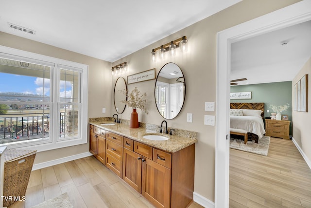 ensuite bathroom with visible vents, wood finished floors, and a sink