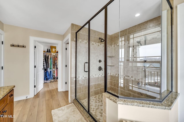 bathroom featuring hardwood / wood-style flooring, a spacious closet, baseboards, and a stall shower