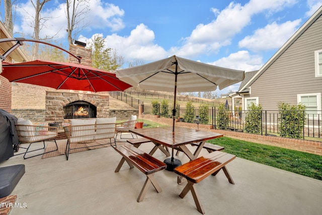 view of patio / terrace featuring outdoor dining space, a lit fireplace, and fence