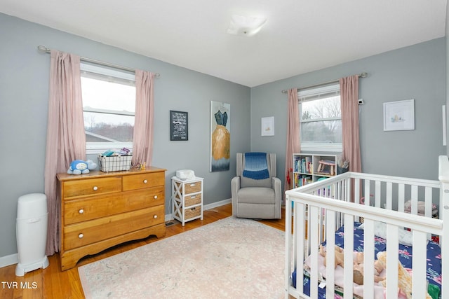 bedroom featuring a crib, baseboards, and wood finished floors