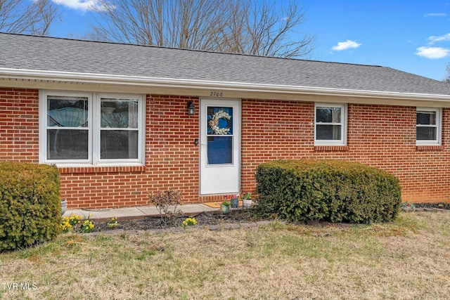 entrance to property featuring brick siding and a lawn