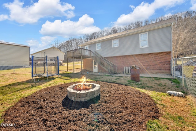 back of house with a trampoline, stairway, an outdoor fire pit, a lawn, and a fenced backyard