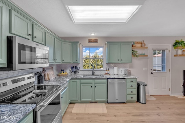 kitchen featuring light stone countertops, stainless steel appliances, green cabinets, and a sink