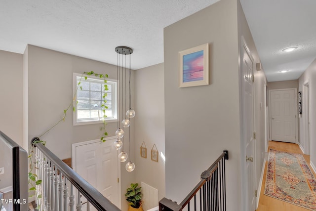 hall with an upstairs landing, light wood-style flooring, and a textured ceiling