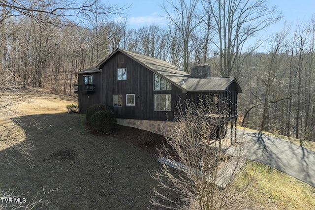 view of side of property featuring a forest view, driveway, and a chimney