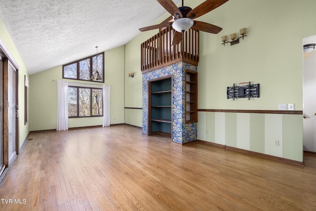 unfurnished living room featuring high vaulted ceiling, a textured ceiling, baseboards, and hardwood / wood-style floors