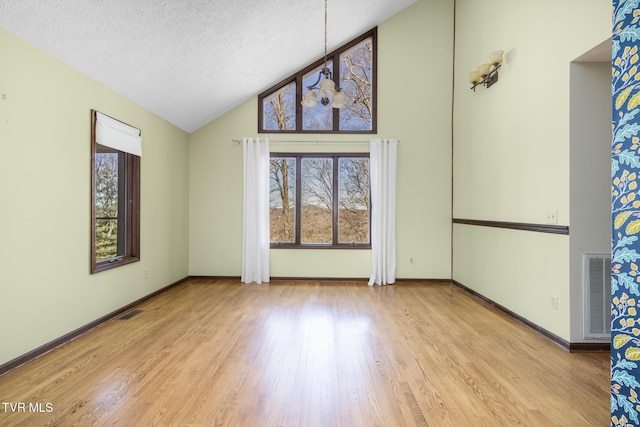 spare room featuring wood finished floors, baseboards, visible vents, high vaulted ceiling, and a textured ceiling