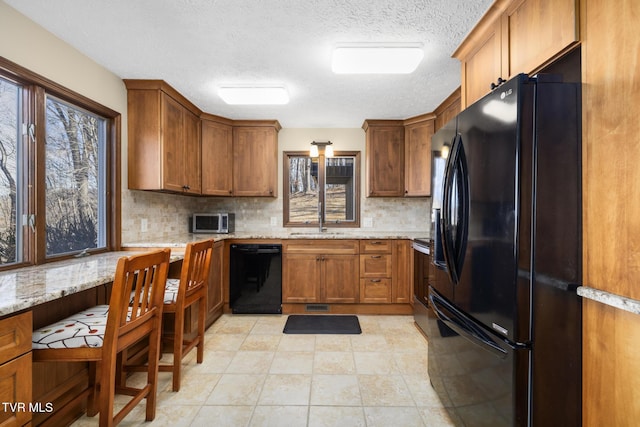 kitchen with black appliances, brown cabinetry, and a healthy amount of sunlight