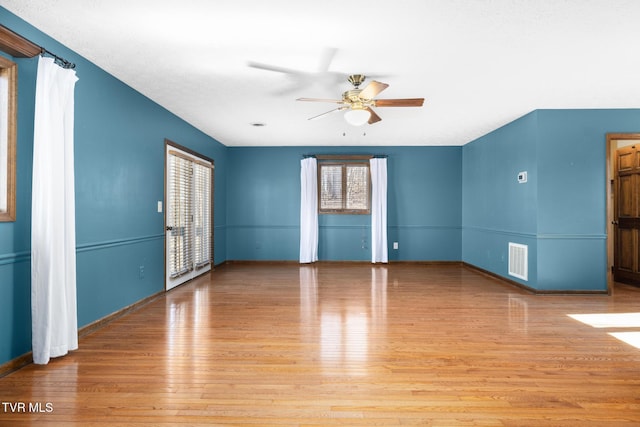 empty room with visible vents, a ceiling fan, baseboards, and wood finished floors