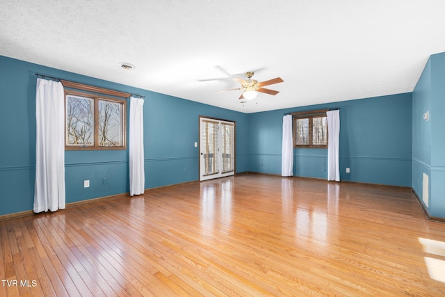 spare room with light wood-style flooring, a ceiling fan, visible vents, and a textured ceiling