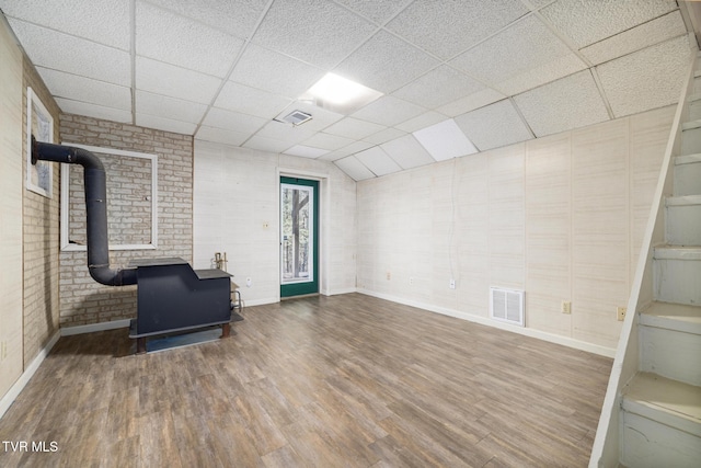 basement featuring a wood stove, wood finished floors, visible vents, and a drop ceiling