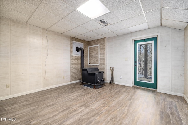 below grade area featuring a drop ceiling, a wood stove, visible vents, and wood finished floors