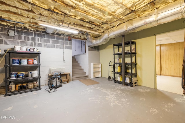 unfinished basement featuring concrete block wall and stairs