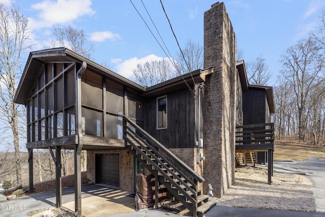 exterior space featuring stairway, driveway, an attached garage, a sunroom, and a chimney