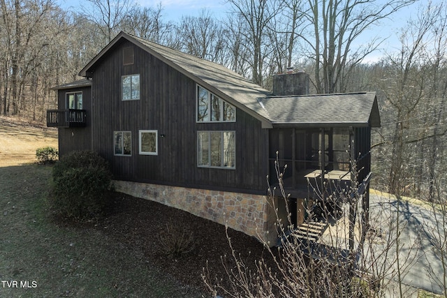 view of side of property with stone siding, a shingled roof, a chimney, and a sunroom