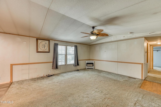 carpeted empty room featuring lofted ceiling, heating unit, a ceiling fan, and a textured ceiling