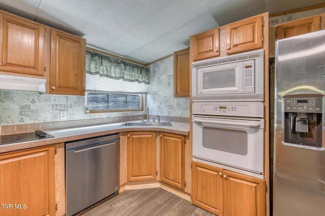 kitchen featuring a sink, under cabinet range hood, a textured ceiling, stainless steel appliances, and wallpapered walls