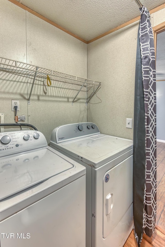 clothes washing area featuring washer and dryer, light wood-style floors, a textured ceiling, and ornamental molding