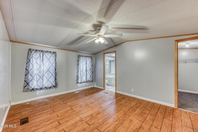 empty room featuring visible vents, light wood-type flooring, ornamental molding, a textured ceiling, and a ceiling fan