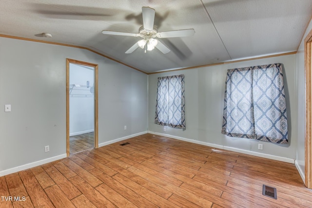 empty room with visible vents, lofted ceiling, light wood-style flooring, a textured ceiling, and a ceiling fan