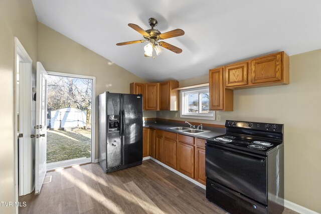 kitchen featuring dark wood-type flooring, lofted ceiling, black appliances, a sink, and baseboards