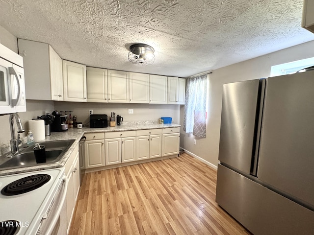 kitchen featuring white microwave, light wood-type flooring, light countertops, freestanding refrigerator, and a sink