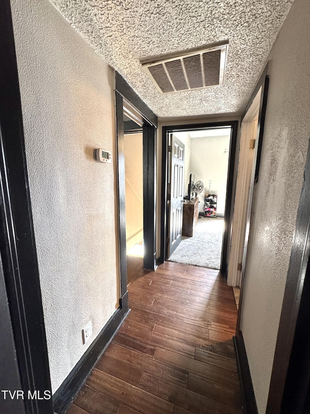 hallway featuring hardwood / wood-style flooring, a textured wall, visible vents, and baseboards