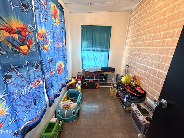 game room featuring brick wall and a drop ceiling