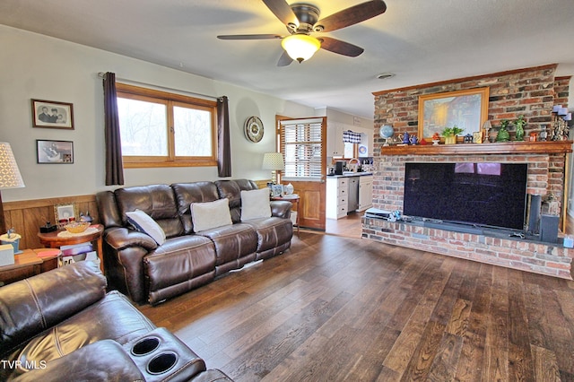 living room with ceiling fan, a brick fireplace, and dark wood-style floors