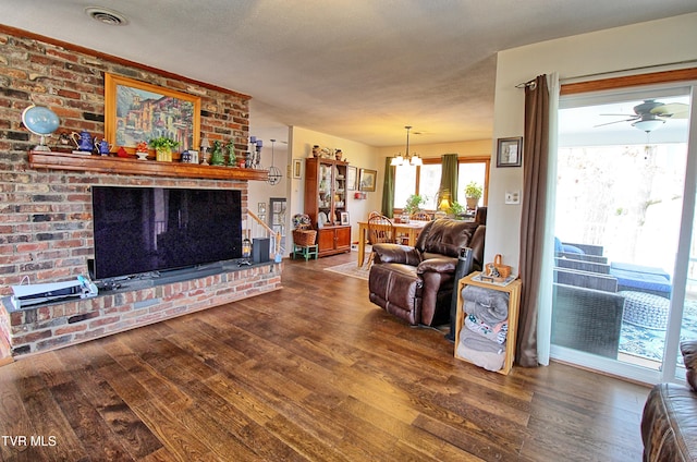 living area featuring wood finished floors, visible vents, a textured ceiling, a brick fireplace, and ceiling fan with notable chandelier