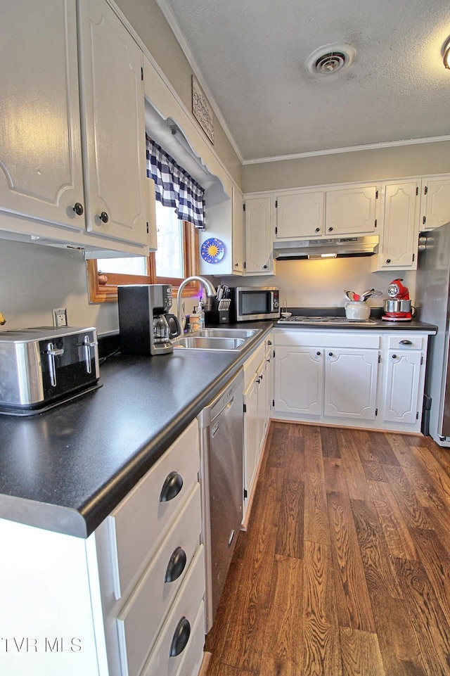 kitchen with dark countertops, under cabinet range hood, appliances with stainless steel finishes, white cabinetry, and dark wood-style flooring