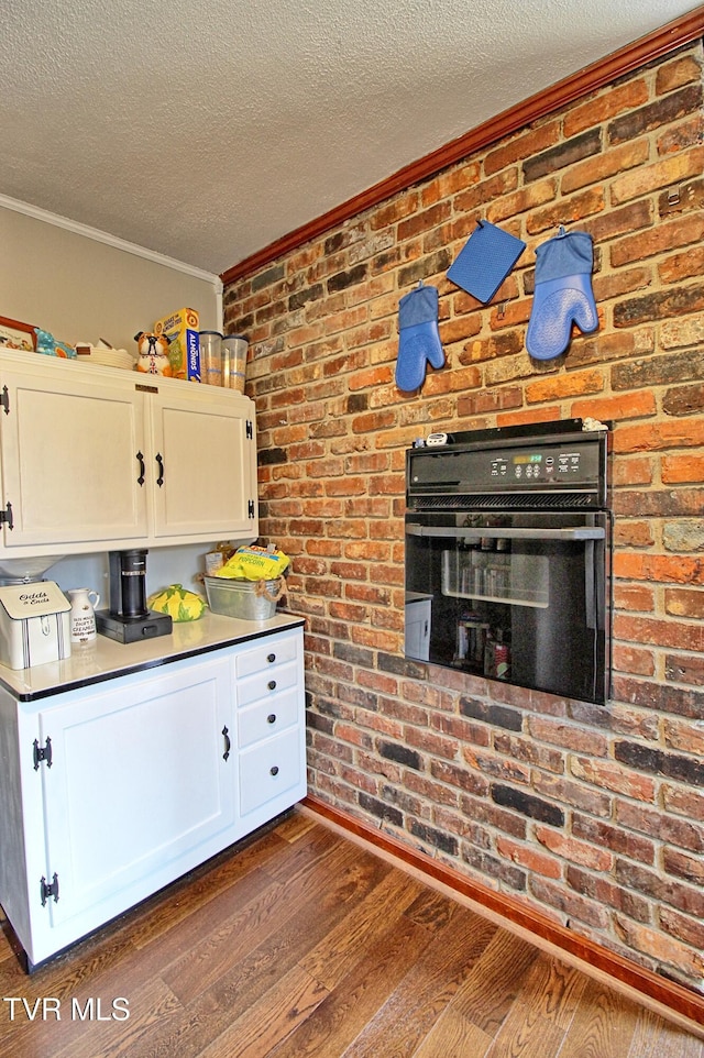 kitchen with dark wood-type flooring, white cabinets, crown molding, and a textured ceiling