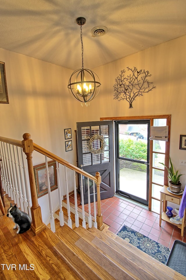 tiled foyer entrance featuring visible vents, stairway, a textured ceiling, and an inviting chandelier