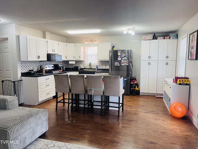 kitchen with a breakfast bar, a kitchen island, white cabinetry, stainless steel appliances, and dark wood-style flooring