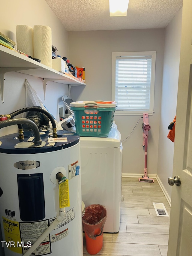 clothes washing area featuring electric water heater, wood finish floors, washer and clothes dryer, laundry area, and a textured ceiling