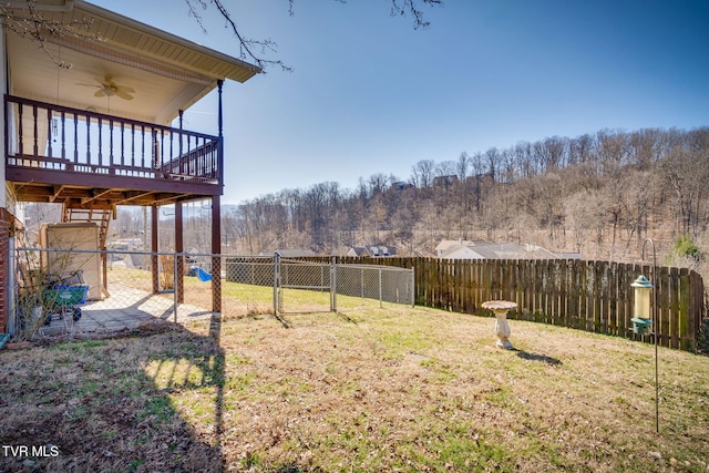 view of yard featuring ceiling fan, a view of trees, a fenced backyard, and a gate