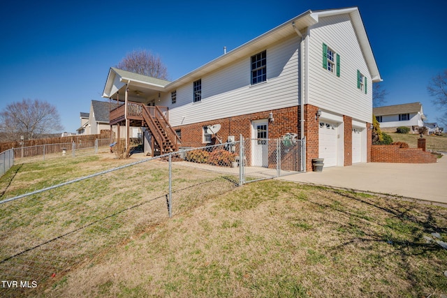 rear view of house with stairway, a yard, concrete driveway, fence private yard, and brick siding