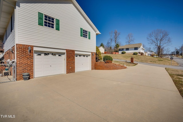 view of side of property featuring a garage, brick siding, driveway, and a yard